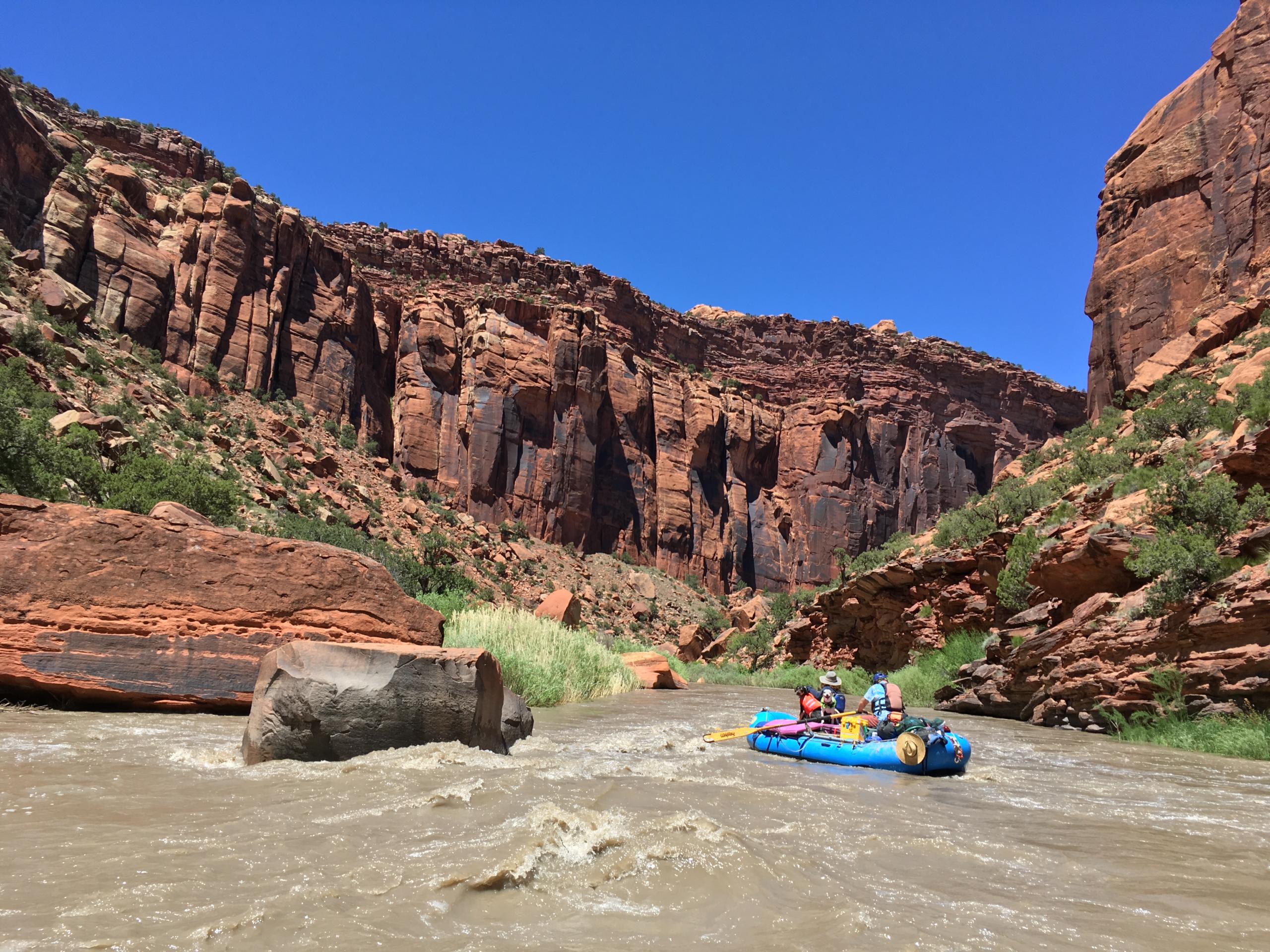 people floating on raft down the winding river surrounded by canyons